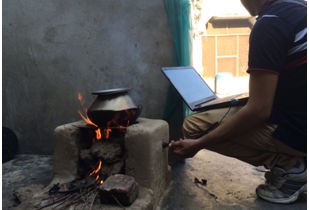A field worker retrieving data from a primary biomass cookstove (chula) fueled with a combination of dung and wood.